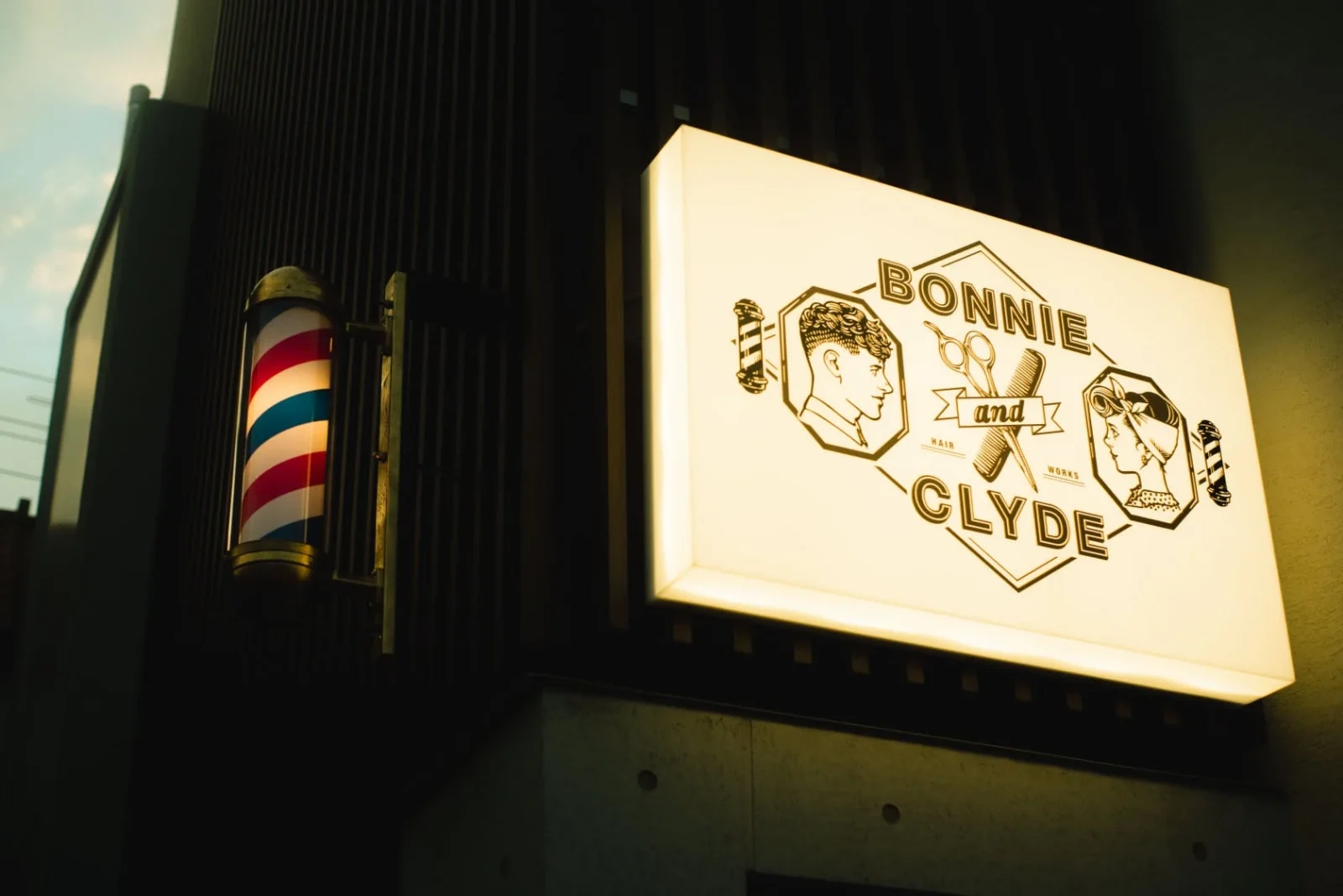 夕暮れの外壁に灯る、BONNIE and CLYDEのロゴ入り看板とサインポール